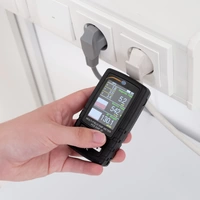 Eine Hand hält ein Leistungsüberwachungsgerät, das Daten von einer Steckdosenleiste misst. Anzeigen zeigen Volt, Ampere, Watt.